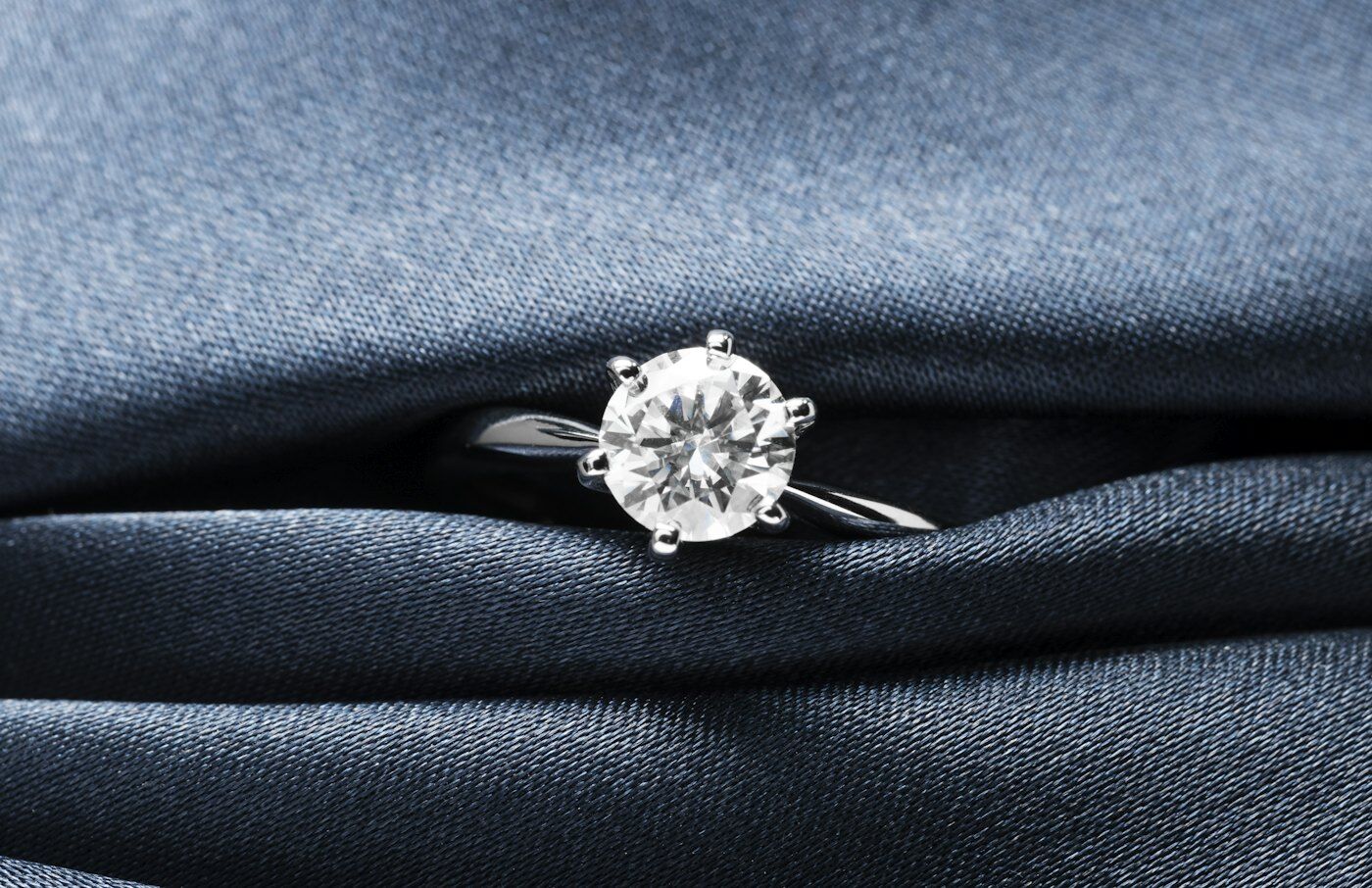 Diamond solitaire ring resting on blue fabric