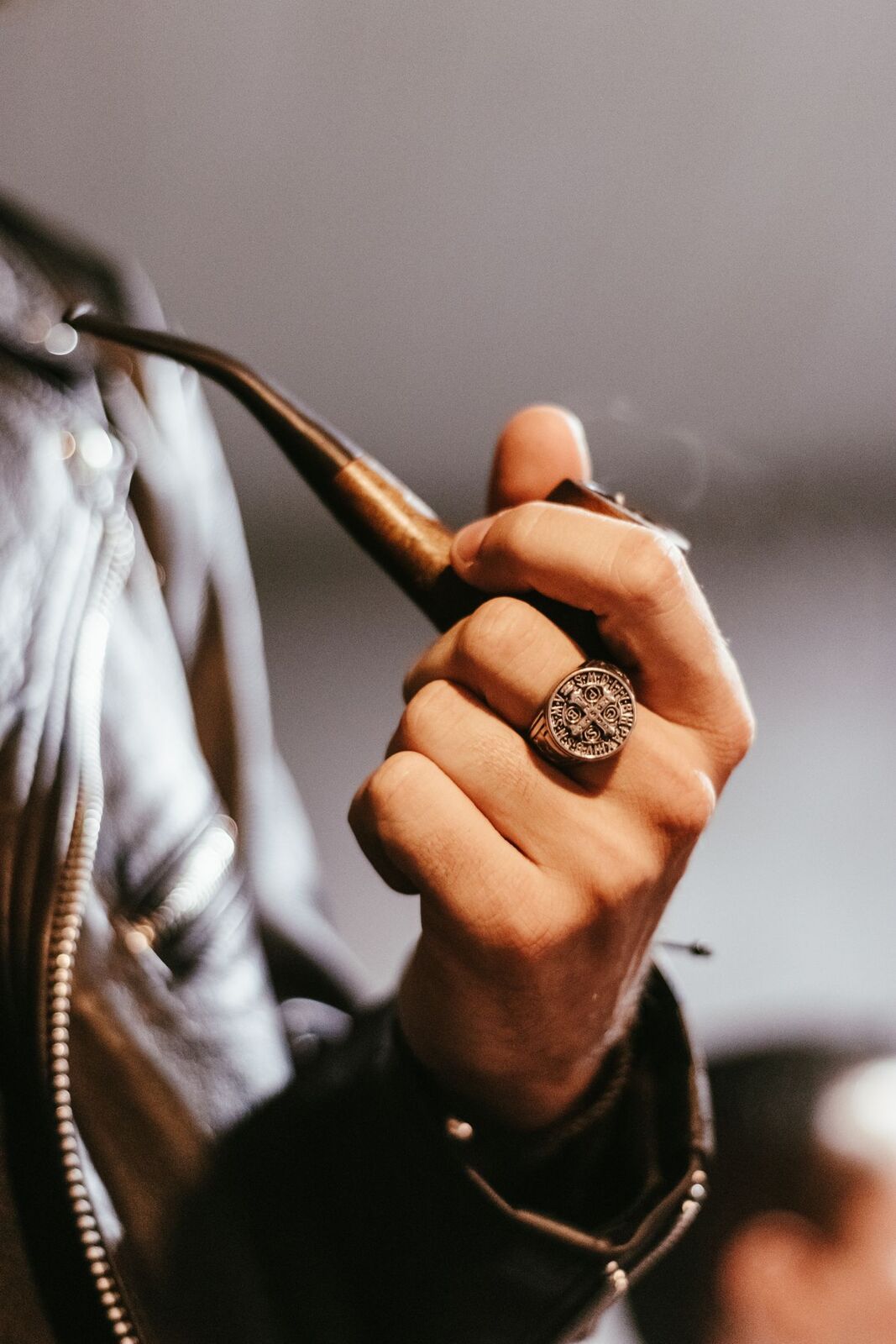 A man's hand wearing a gold signet ring, holding a pipe